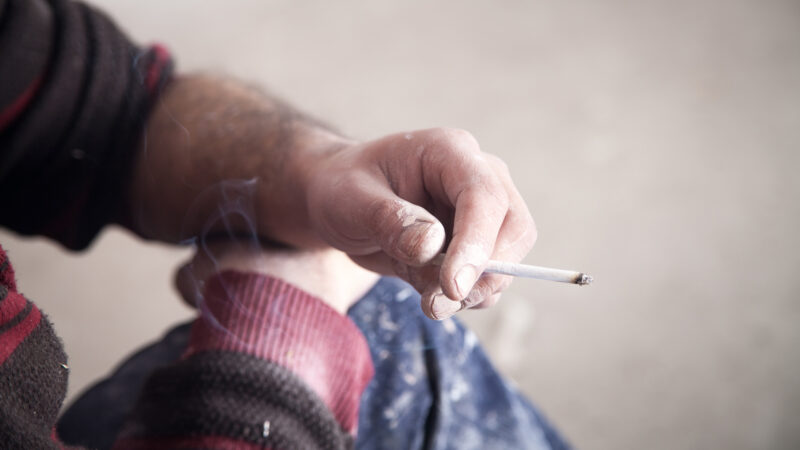 Billedet viser en hånd, som holder en tændt cigaret