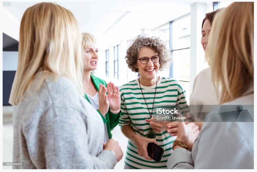På billedet ser man 4 mennesker stå i en gruppe og have en dialog - de smiler og er glade